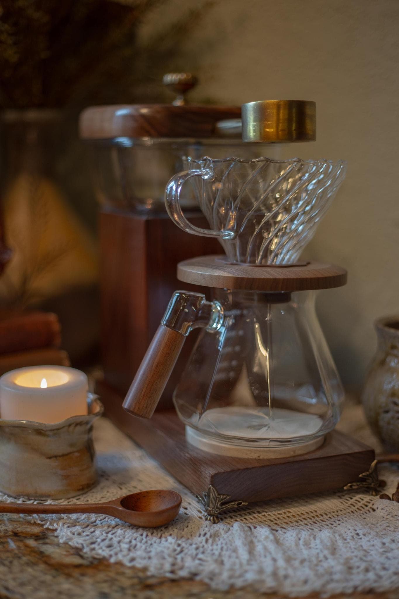 The Heritage Drip by candlelight on a lace cloth, a wooden spoon at its feet and the brass scoop catching the flame